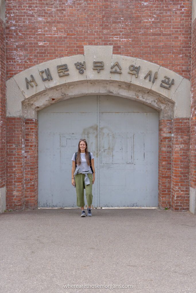 Woman standing inside a gate underneath a brick archway