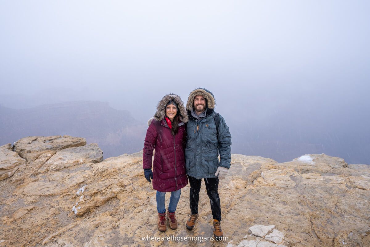 Couple standing together on a rocky outcrop in winter coats with a misty haze behind