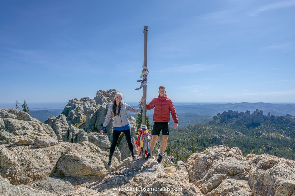 Couple holding onto a flagpole at the summit of a rocky trail on a clear day