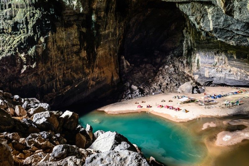 Several campsite scattered around a body of water inside hang en cave