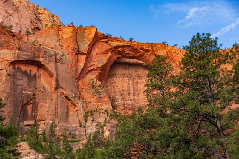 Enormous natural sandstone arch eroded into a tall red rock cliff with blue sky behind
