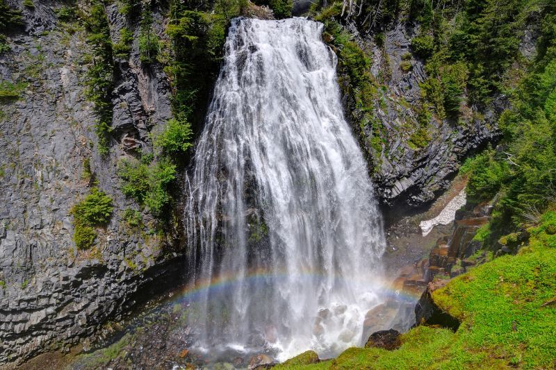 Wide waterfall crashing into a ravine with a colorful rainbow at the bottom