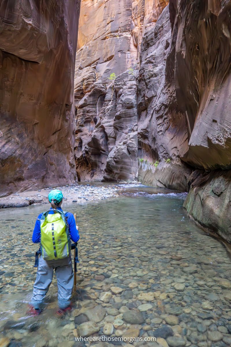 Hiking in waterproofs holding a pole and standing in a narrow river slot canyon in Utah, USA