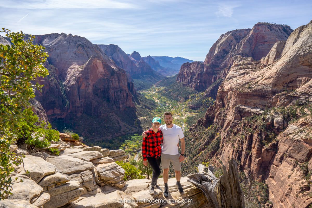 Couple standing together at the summit of Angels Landing Trail in Zion on a clear sunny day with huge canyon views behind