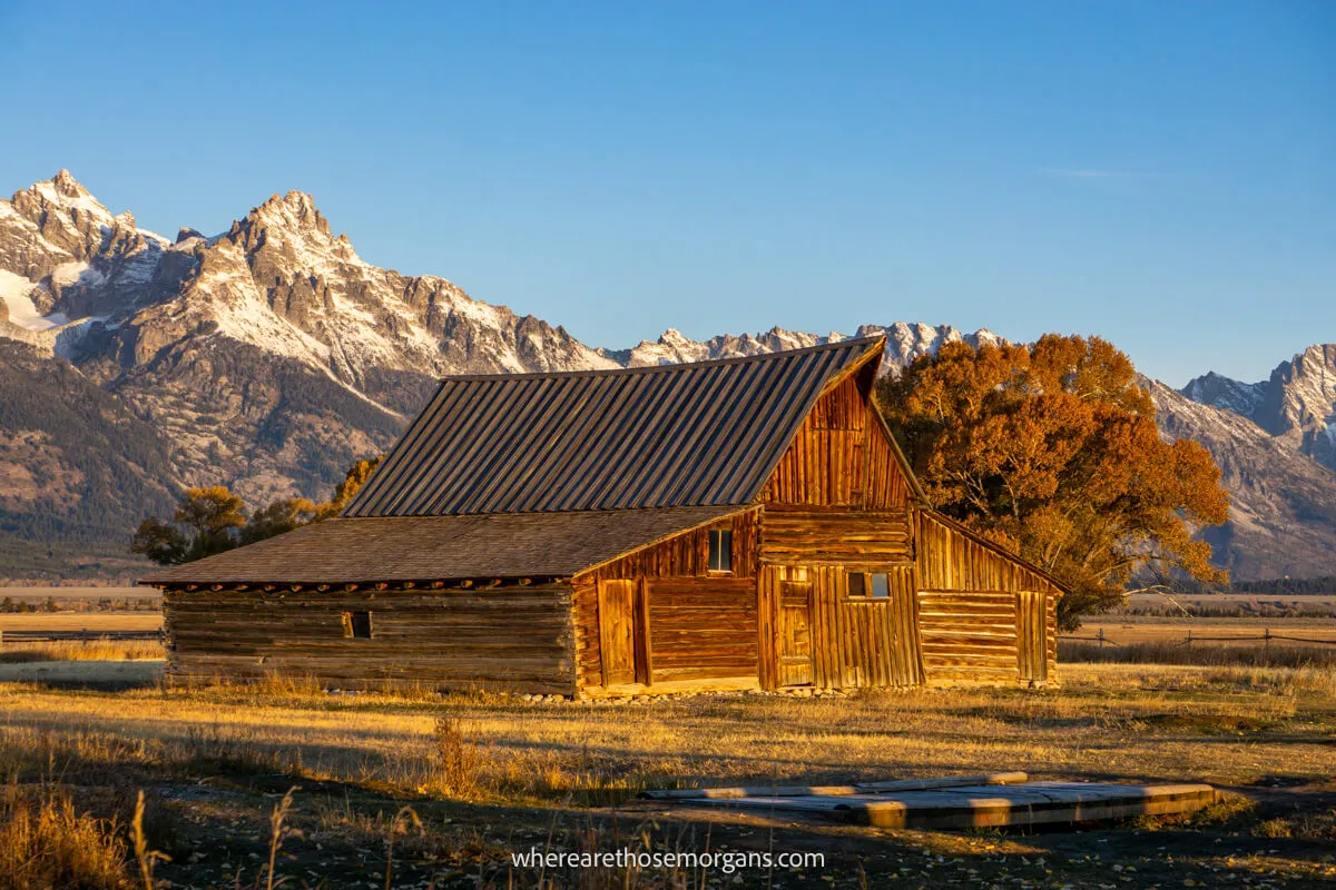 Wooden barn lit up by sunlight at sunrise with mountains in the background