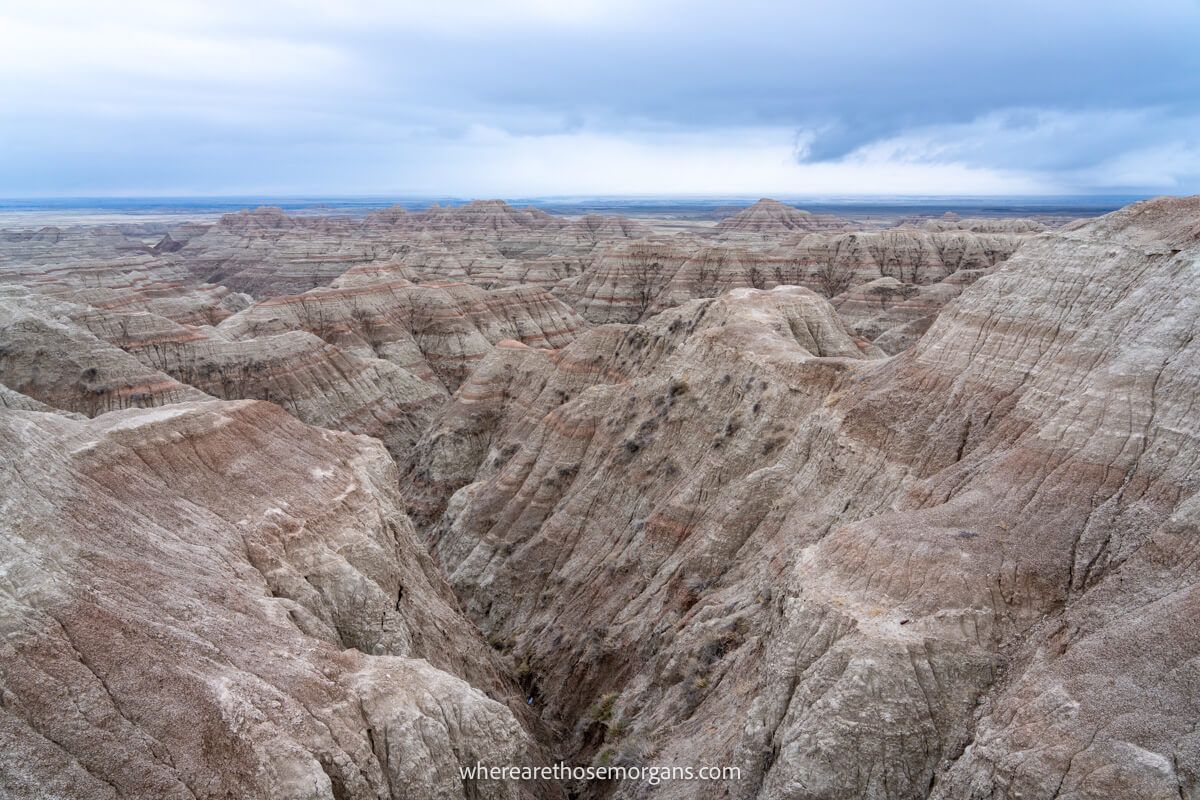 Wide open landscape filled with dramatic ravines and buttes with colorful rock layers and thick clouds in the sky