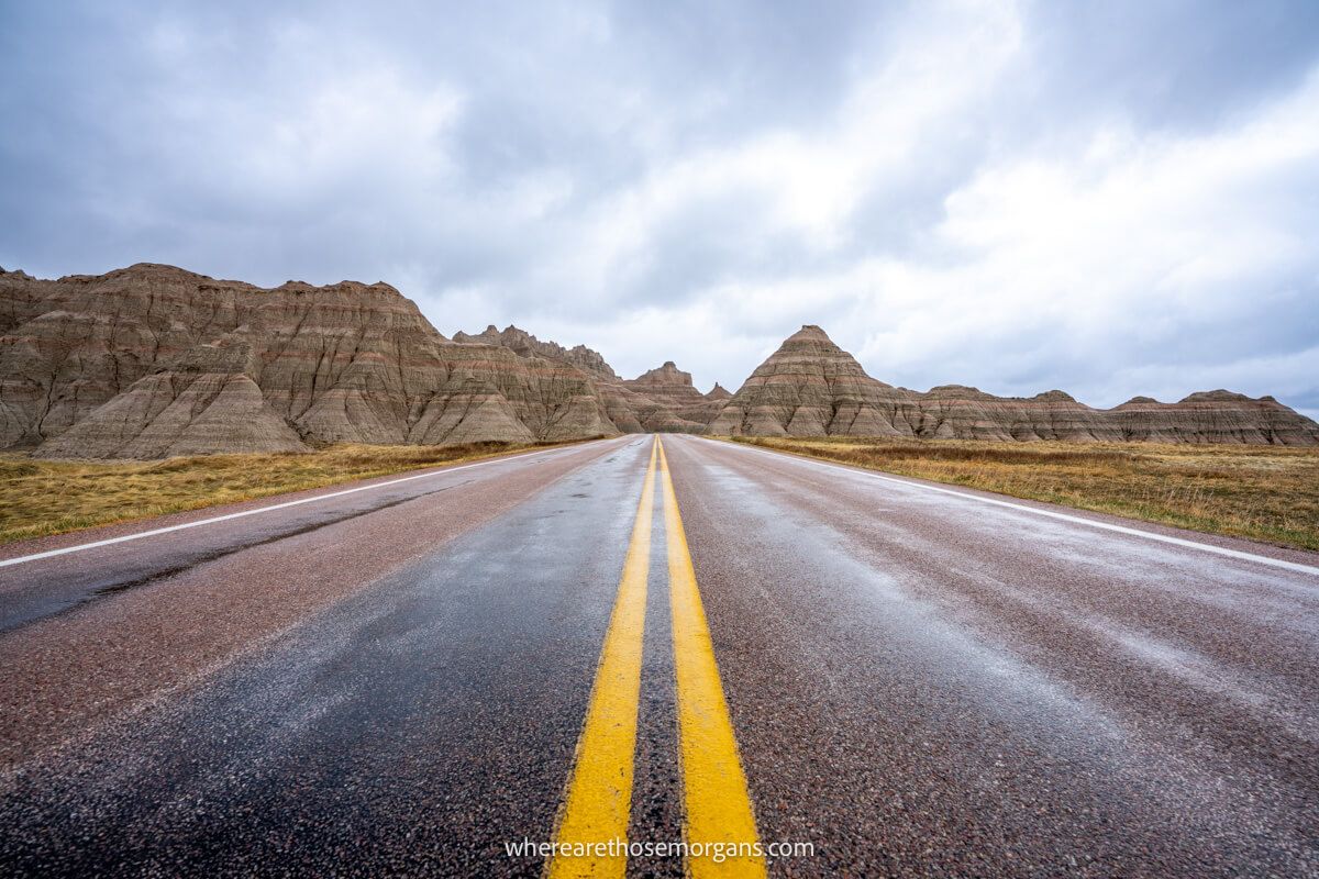 Photo of a road with yellow lines running straight ahead and disappearing into rock formations with heavy clouds in the sky