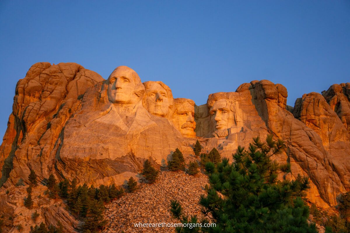 Mount Rushmore glowing orange at sunrise with a deep blue clear sky behind