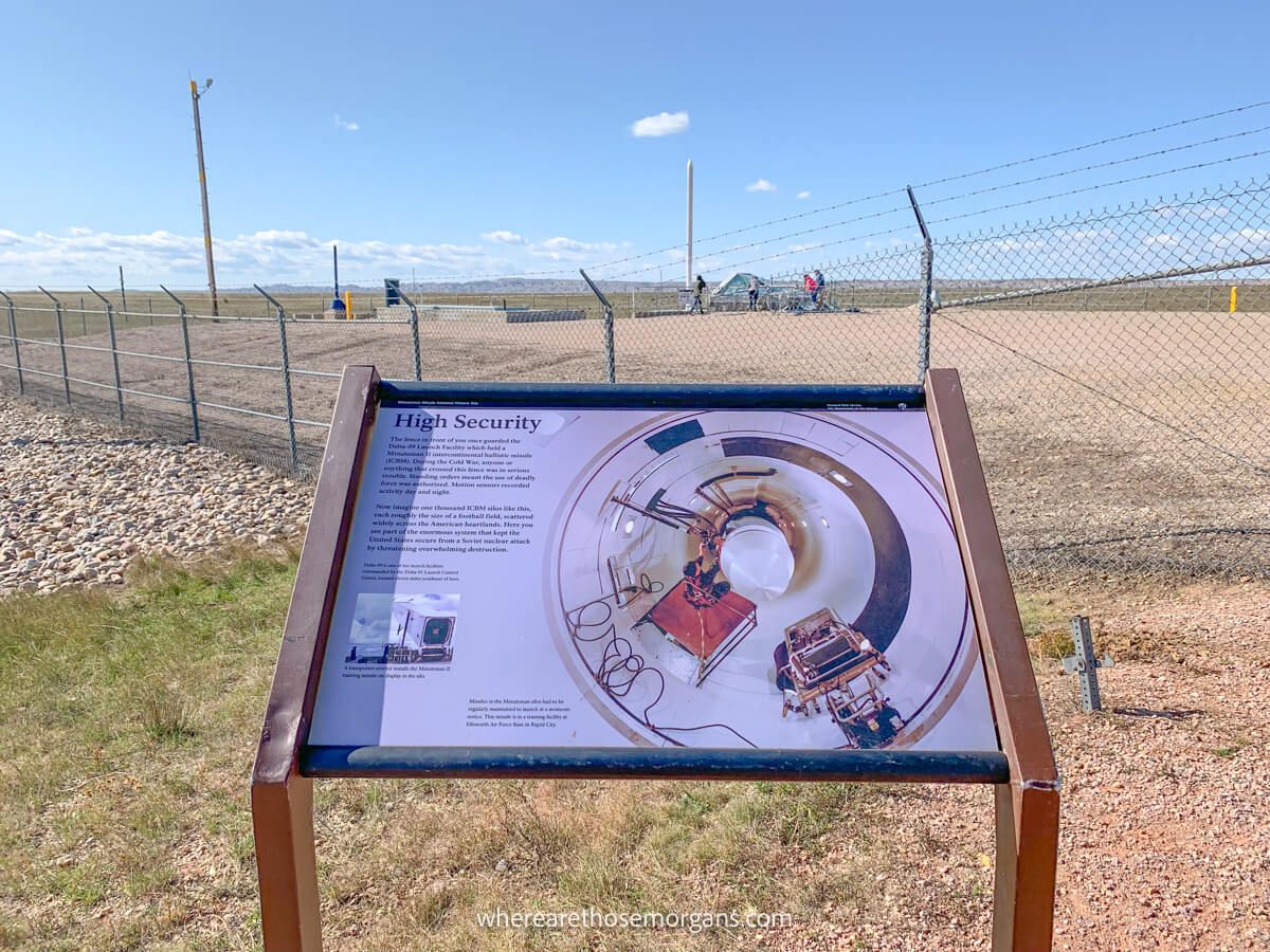 Information board showing the inside of a missile silo in front of the actual location of the silo with fencing on a clear day