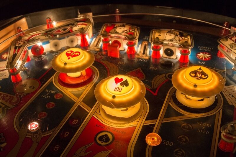 Close up photo of the inside of a pinball machine dimly lit with brighter lights on the bumpers