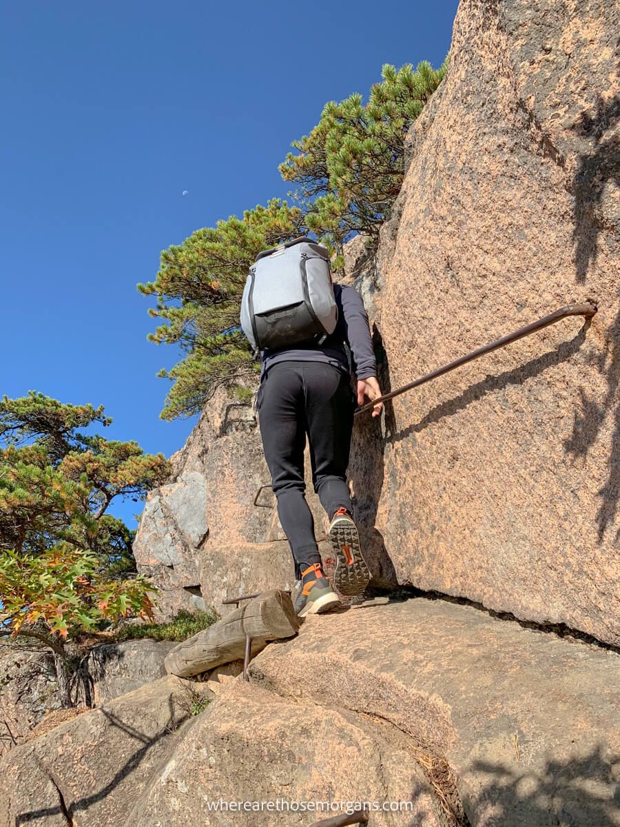 Hiker scrambling up steep rocks with metal ladders and rails