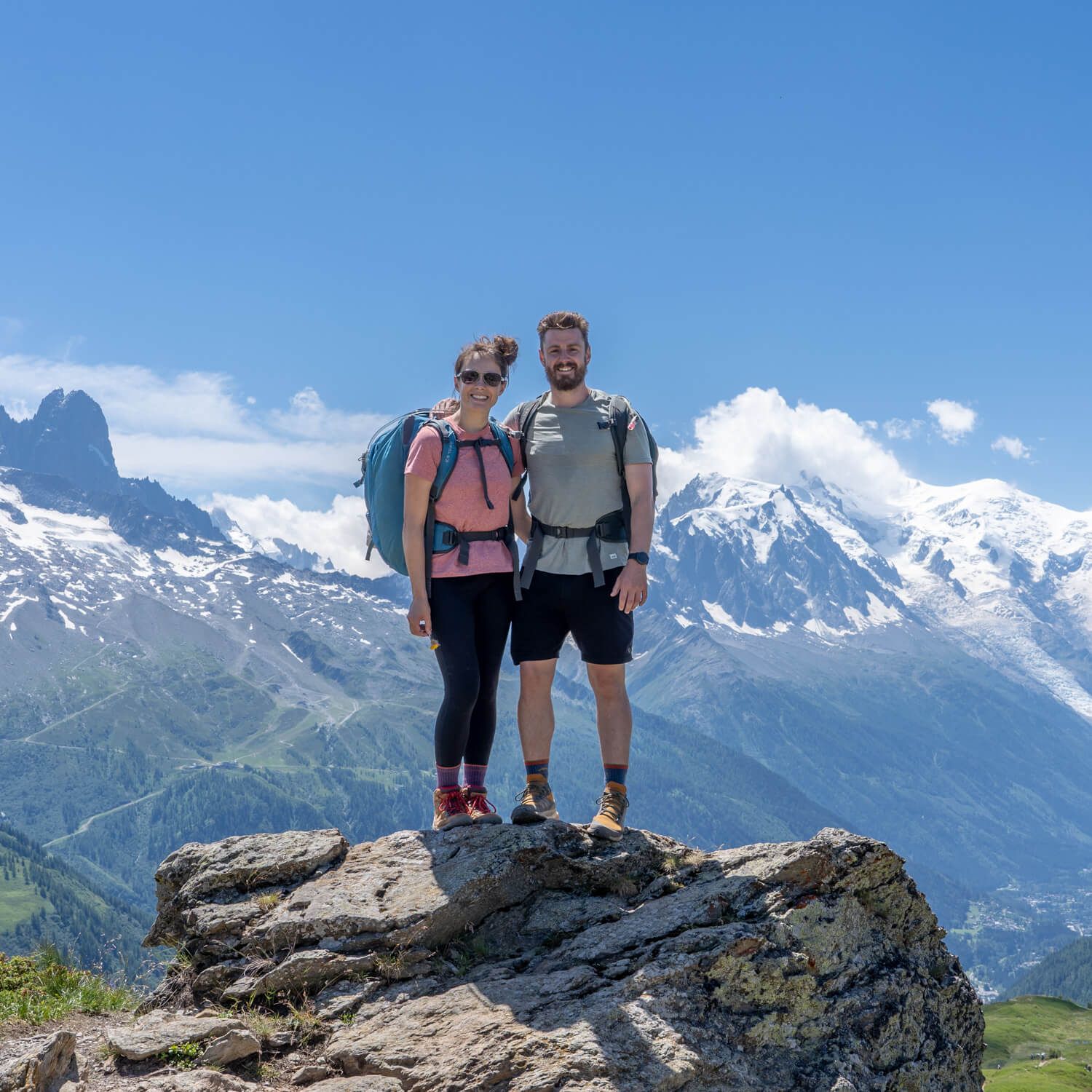 Photo of Mark and Kristen from Where Are Those Morgans standing together on a rock in hiking gear with backpacks and snow capped mountains behind on a clear day