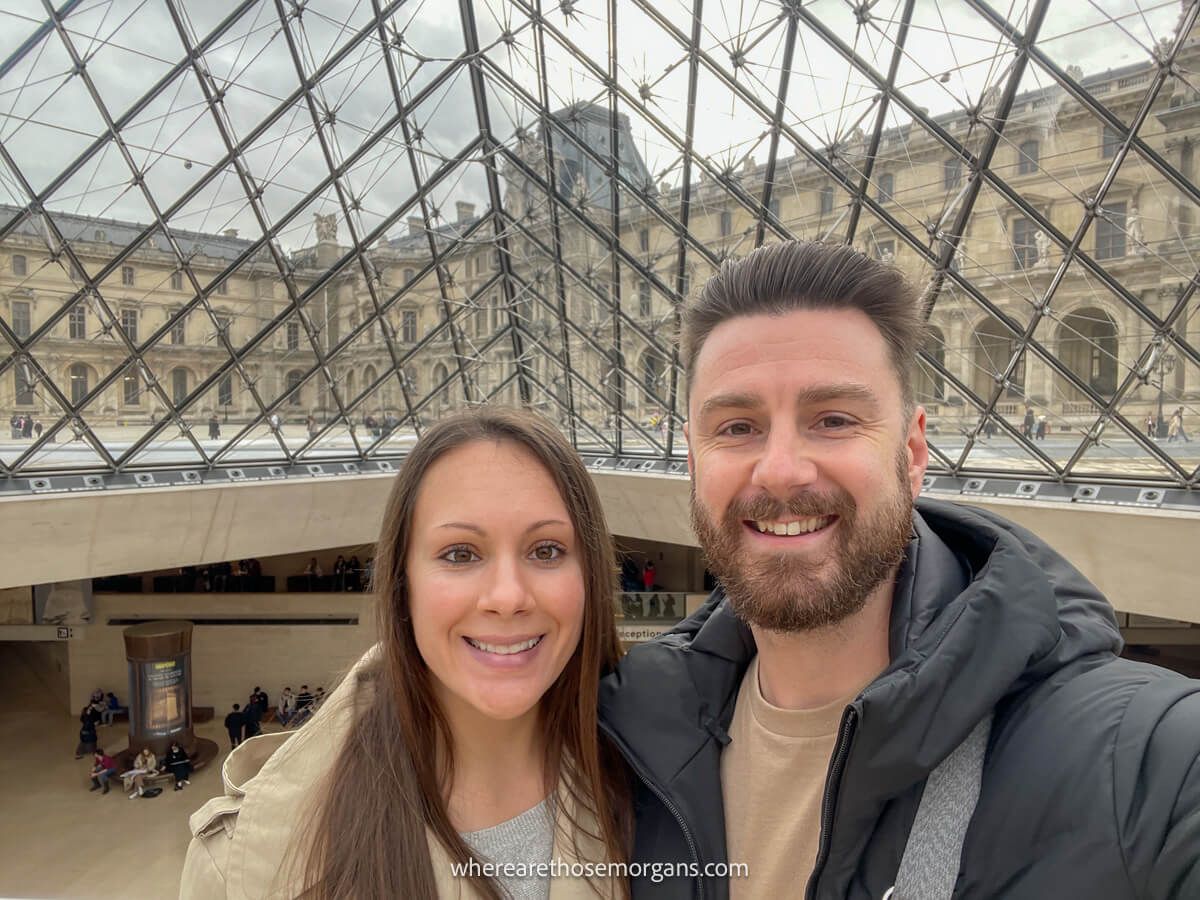Man a women taking a selfie at the entrance of the Louvre