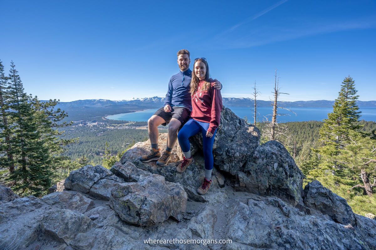 Couple hugging on a rock with elevated views over a body of water behind