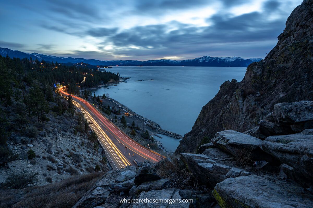Photo of Lake Tahoe at night with car light trails both white and red passing underneath on the road