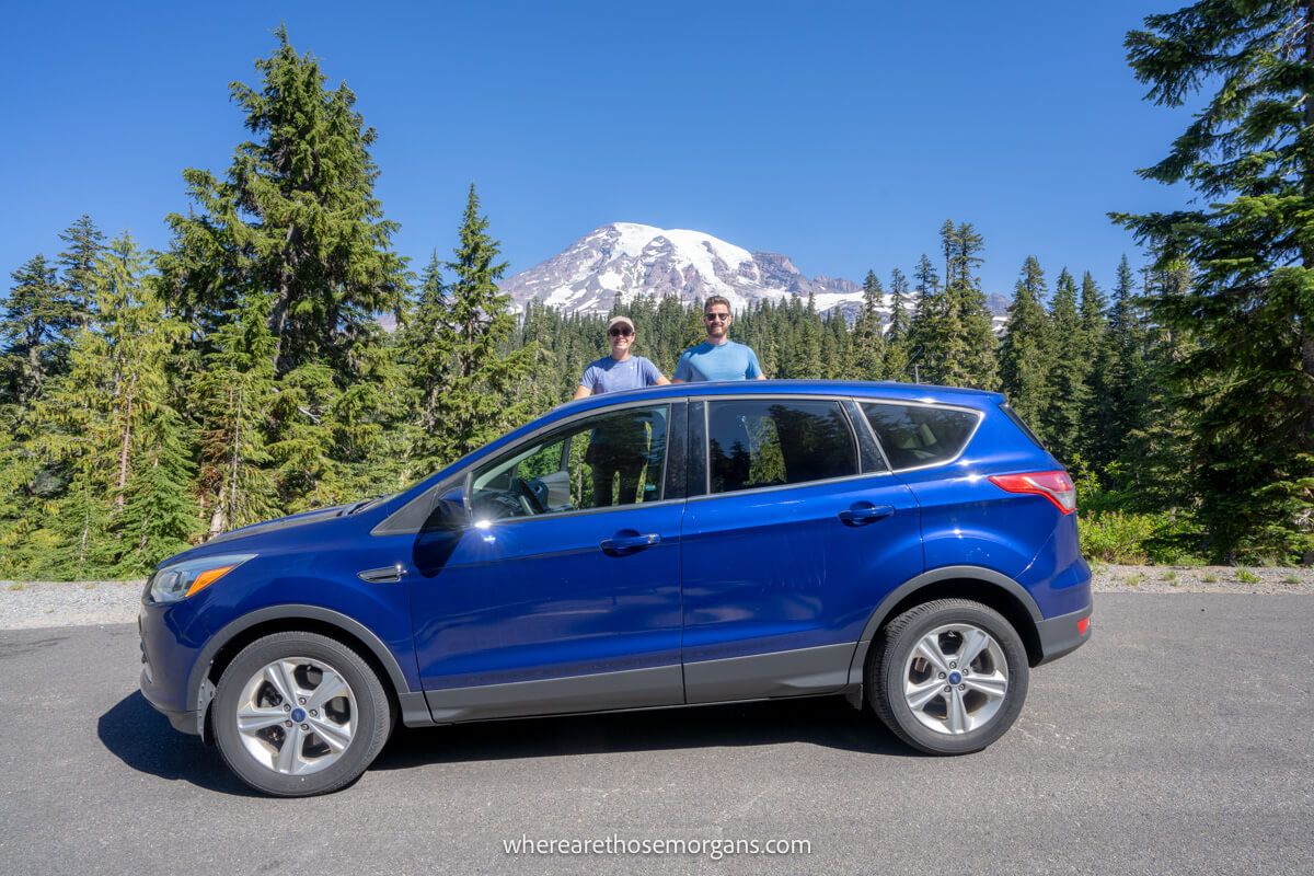 Man and woman posing for a photo with their car in front of Mount Rainier