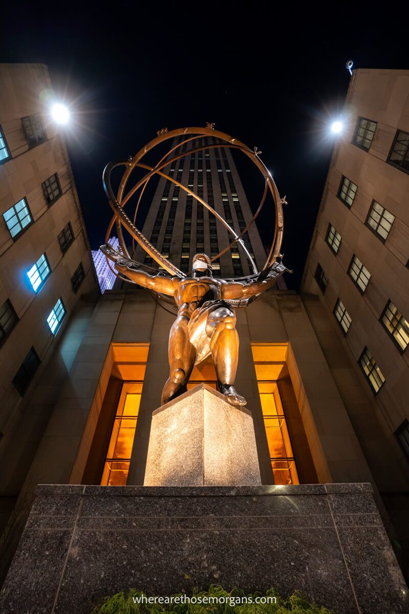 Statue of Atlas lit up with orange light from below at night in NYC
