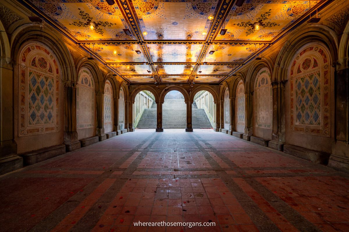 The inside of a tiled terrace with intricate artwork leading to a set of stairs and daylight through two columns Bethesda Terrace one of our favorite NYC photo spots