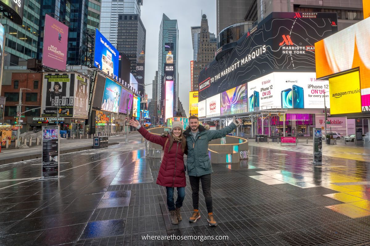 Couple standing together with nobody else around in Times Square NYC with advertising boards flashing
