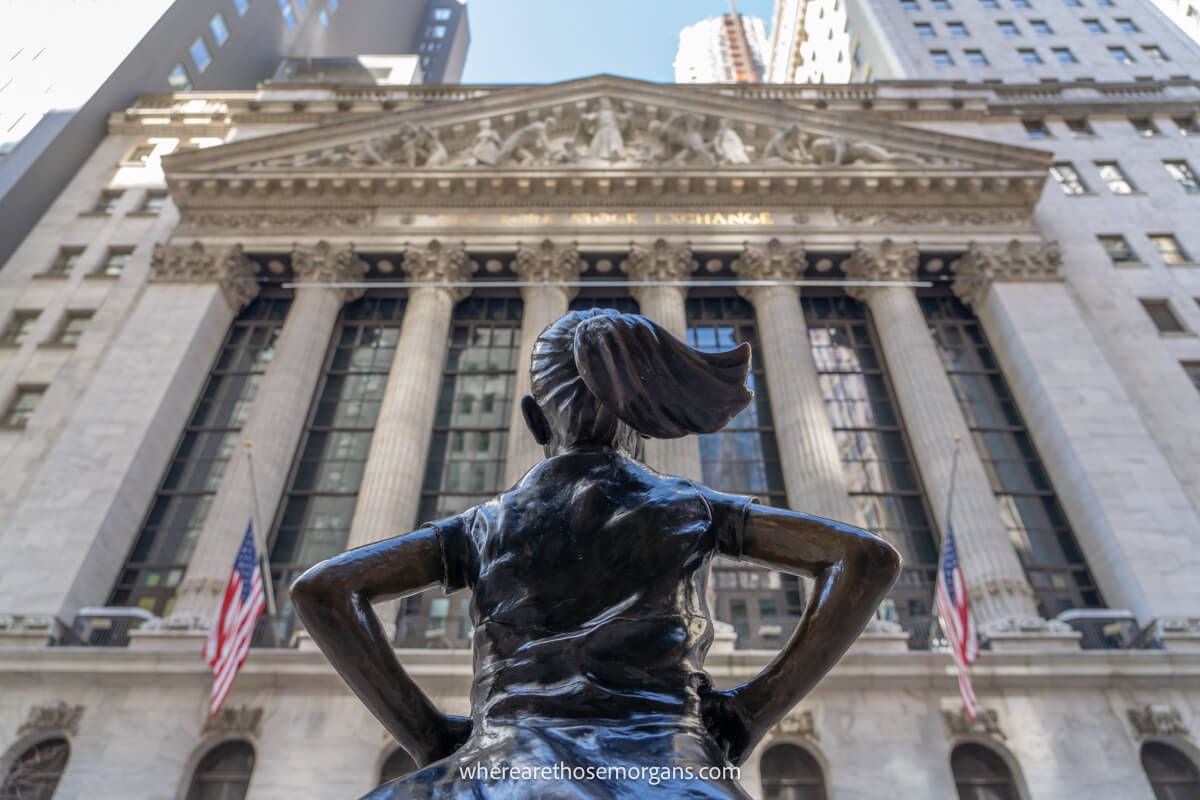 Small statue of a person looking up at the New York Stock Exchange