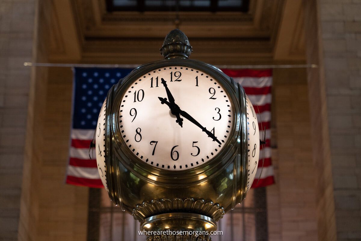Four sided clock with an American flag behind in a grand hall
