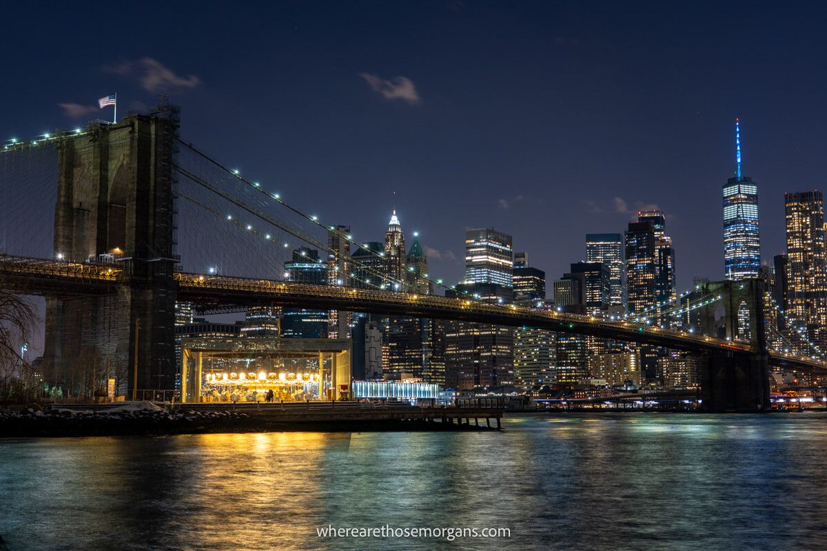 Carousel underneath Brooklyn Bridge crossing the East River with Lower Manhattan in the background at night