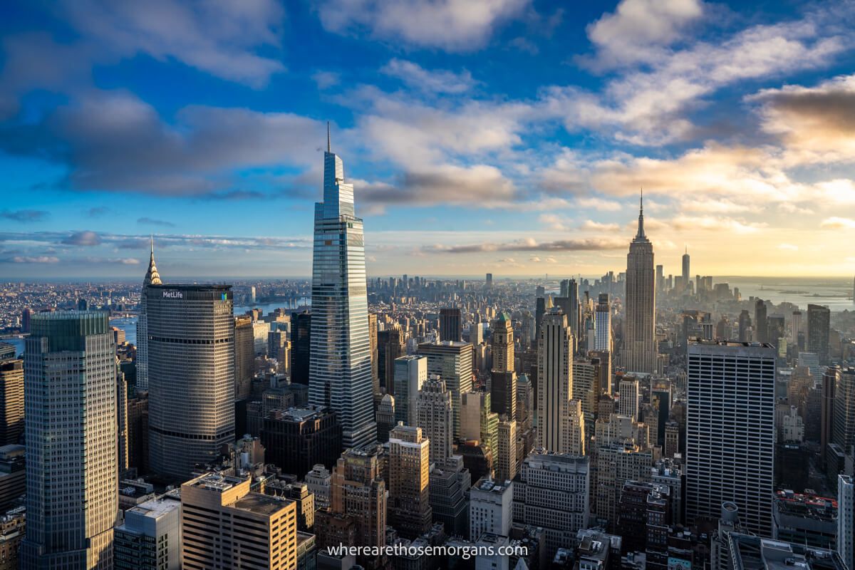 The New York City skyline from Top of the Rock observation deck in late afternoon with clouds in the sky and the city lit up with soft sunlight