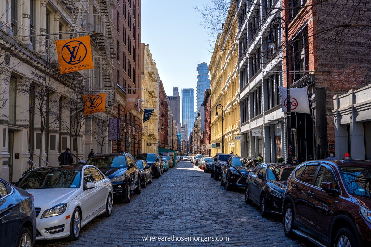Cobbled street with cars parked on either side and boutique stores at the bottoms of tall buildings