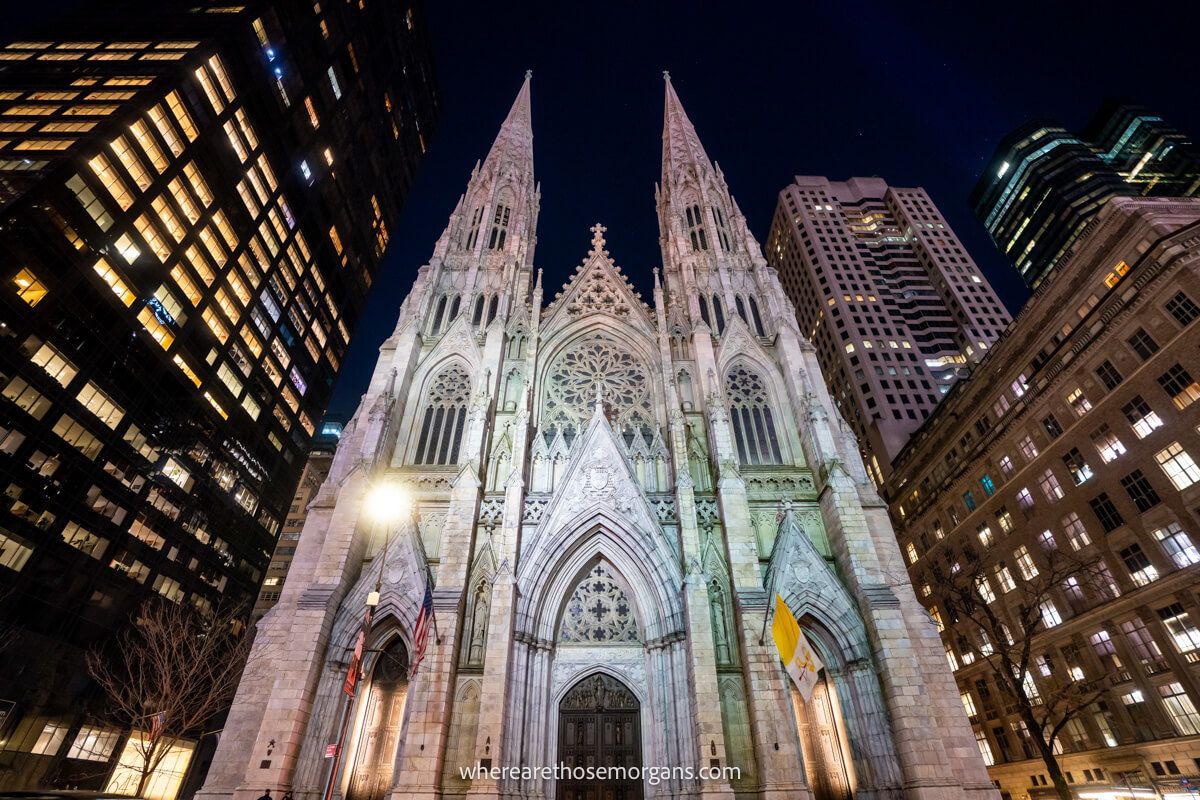 Cathedral lit up at night in a city with tall buildings around