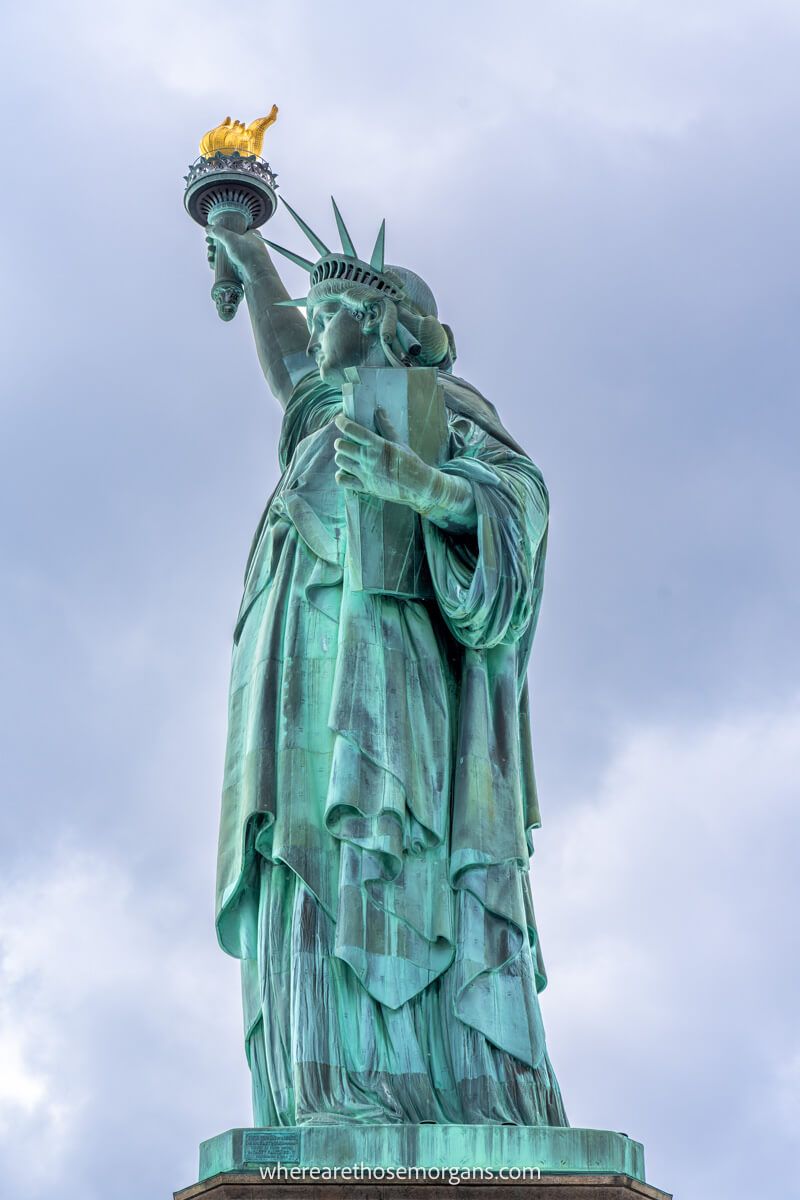 Close up on a side profile of the Statue of Liberty holding her torch aloft into a cloudy sky