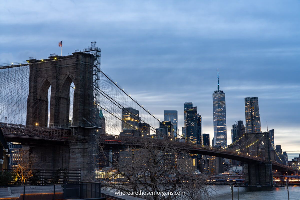 Close up photo of a bridge crossing a river into New York City with skyscrapers at dusk