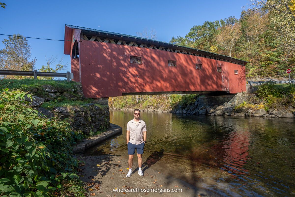 Man standing under a wooden covered bridge on a sunny day in fall