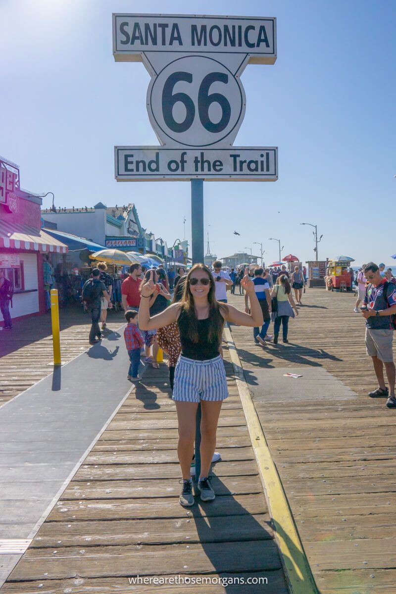 Woman standing under the end of Route 66 trail sign on the Santa Monica Pier in Los Angeles