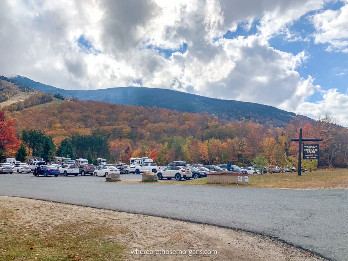 Large parking lot with rolling hills behind covered in bright fall foliage colors on a cloudy but sunny day