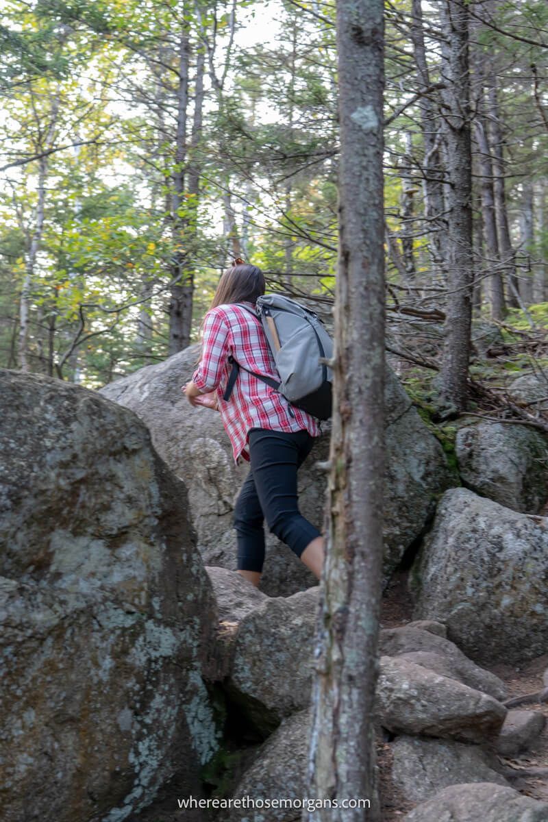 Hiker in a plaid shirt walking up large stones through a forest