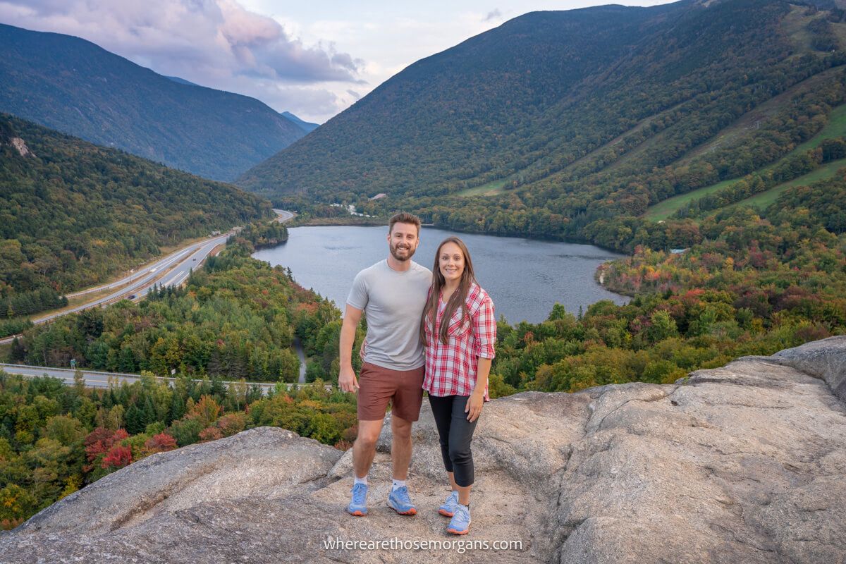 Couple standing together for a photo on a rocky outcrop called Artists Bluff with views behind over a lake and rolling hills covered in trees