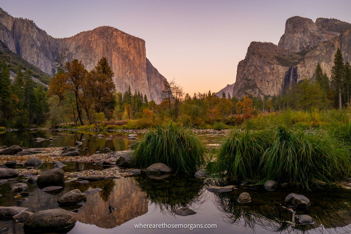 View of a still river with vegetation leading to a wide open valley flanked by tall granite monoliths at sunrise in Yosemite National Park at the end of October