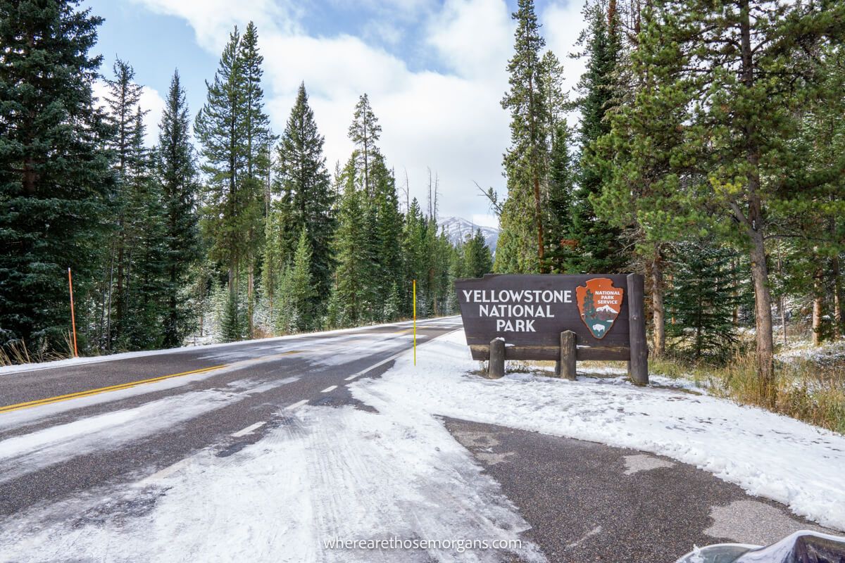 Entrance sign to Yellowstone National Park in October with snow on the ground and evergreen trees contrasting against a blue sky