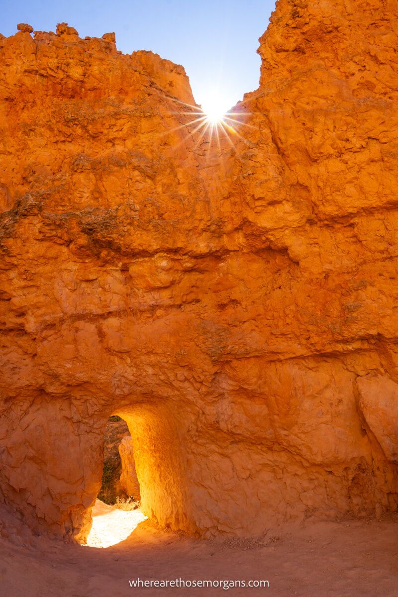 Photo of a sandstone wall with a human-made doorway carved out and the sun bursting over the top of the wall