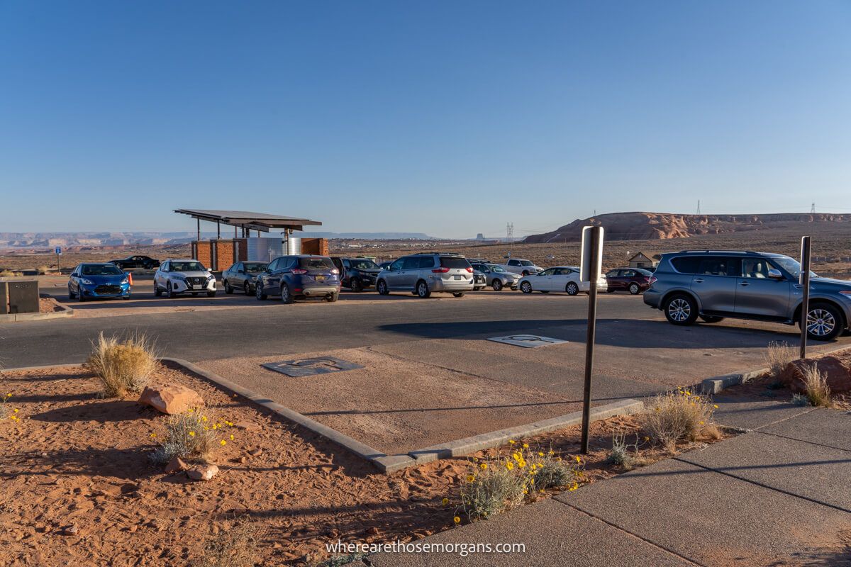 Large parking area with cars parked next to a sandy path with a clear blue sky above