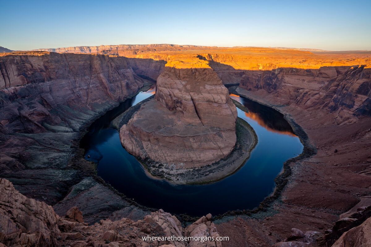 Photo taken from above looking down over a natural geological formation in Arizona called Horseshoe Bend, a huge 270-degree curve in the Colorado River at sunrise with heavy contrasts between highlights and shadows