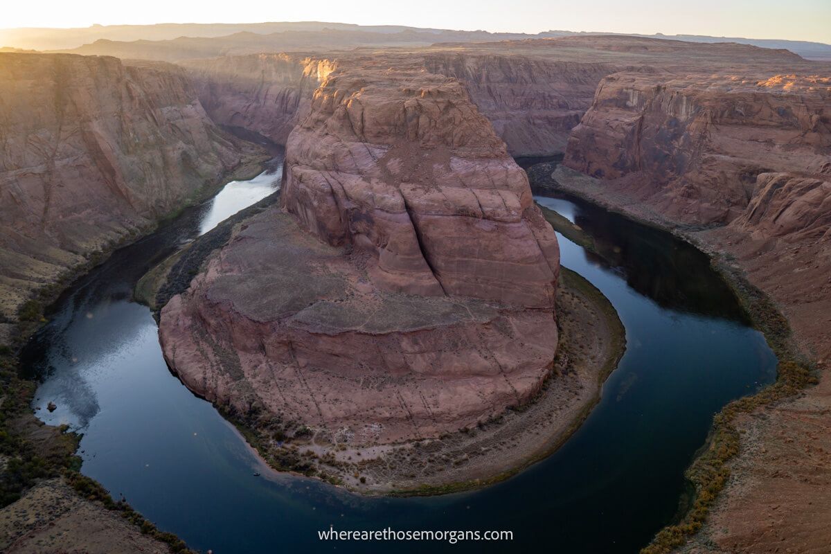 Photo looking down at a U-shaped bend in a river deeply carved into tall cliffs at Horseshoe Bend AZ during sunset
