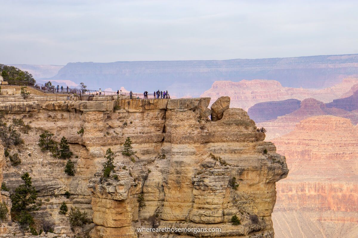 Tourists on a rocky cliff in a fenced-in area surrounded by deep rock formations at dawn