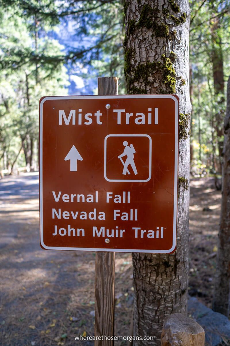 Brown sign showing directions to a hike and landmarks in a forest