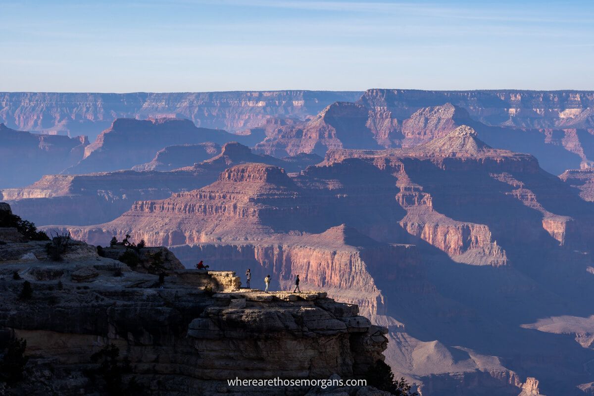 Rocky outcrop with people standing in a fenced area overlooking a striking and wide open rocky landscape at dusk