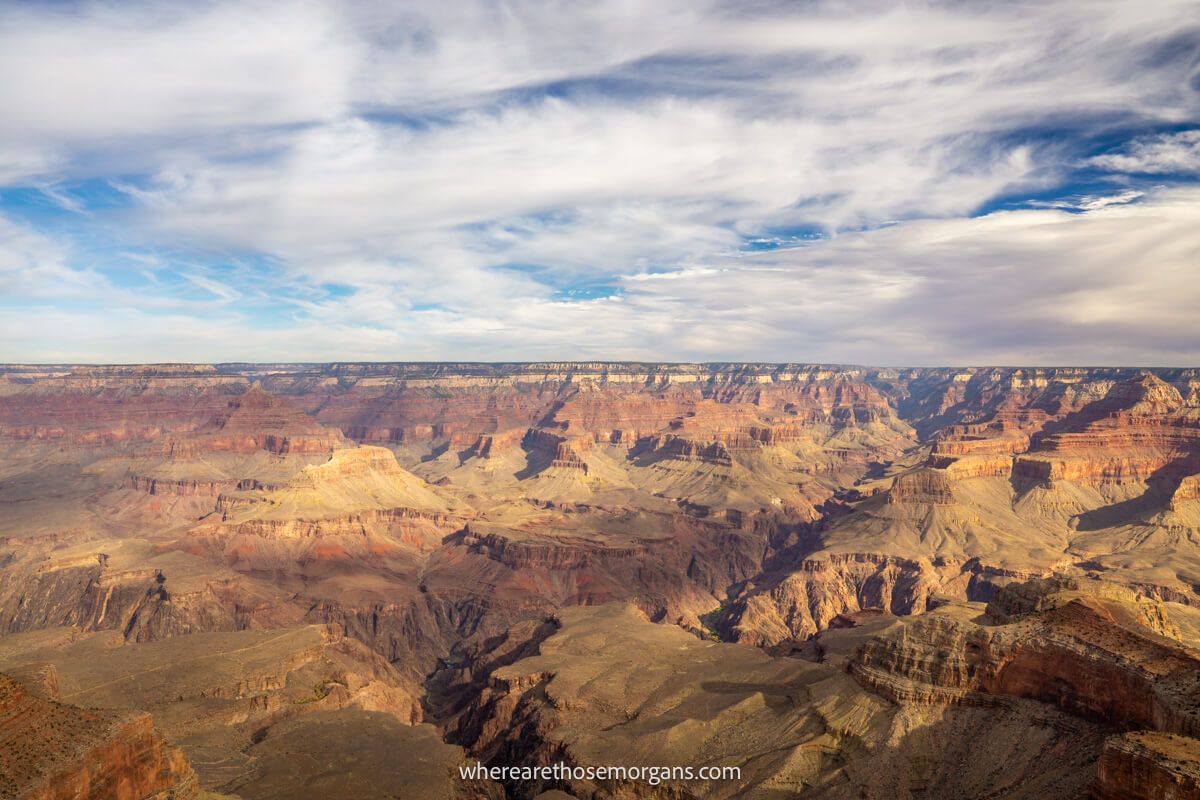 Rugged and jagged rock formations inside a vast canyon stretching as far as the eye can see with light puffy clouds in the sky