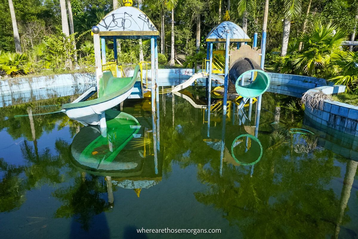 An old children's pool with two slides and murky brown water