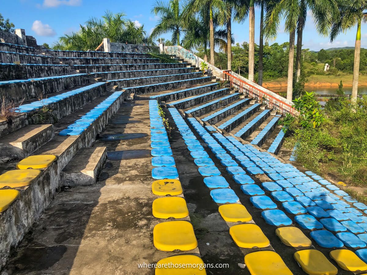 An abandoned amphitheater with yellow and blue seats alongside a lake