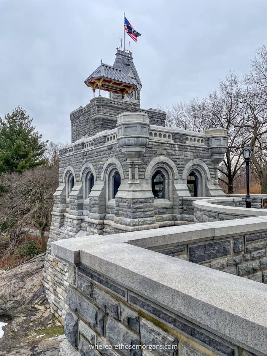 Photo taken on a diagonal angle of a small castle exterior with walls, turret and flag flying on a cloudy day