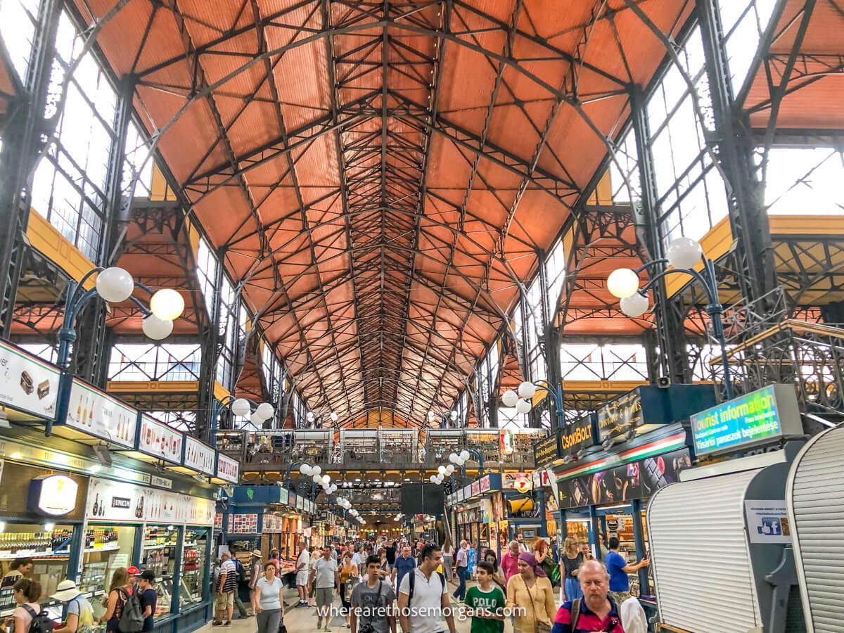 The inside of a market in Budapest with orange canopy above lots of shoppers and tourists at stalls